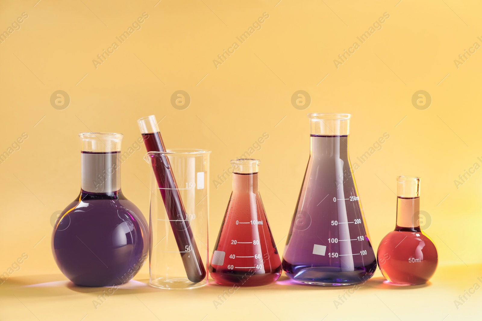 Laboratory glassware with colorful liquids on beige background Photo of Laboratory glassware with colorful liquids on beige background