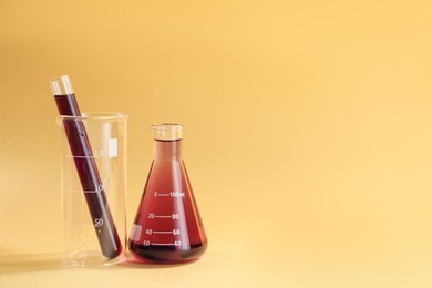 Photo of Laboratory glassware with colorful liquids on beige background. Space for text