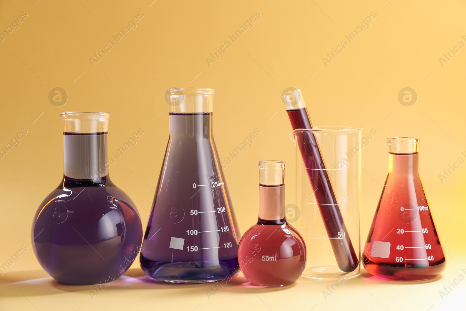 Laboratory glassware with colorful liquids on beige background Photo of Laboratory glassware with colorful liquids on beige background
