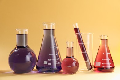 Photo of Laboratory glassware with colorful liquids on beige background