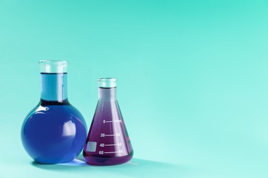 Photo of Laboratory glassware with colorful liquids on turquoise background. Space for text