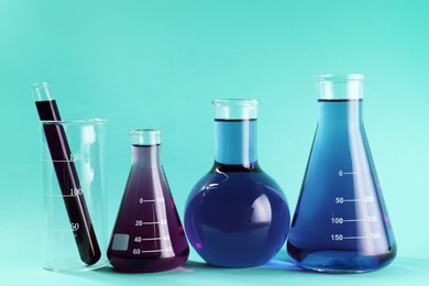Photo of Laboratory glassware with colorful liquids on turquoise background