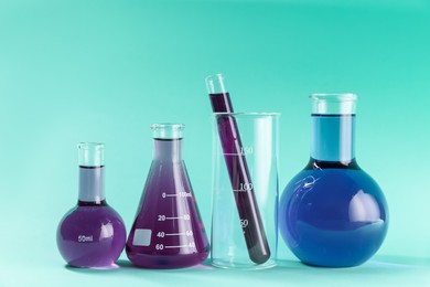 Photo of Laboratory glassware with colorful liquids on turquoise background