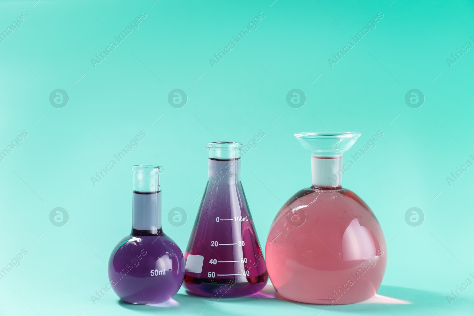 Laboratory glassware with colorful liquids on turquoise background. Space for text Photo of Laboratory glassware with colorful liquids on turquoise background. Space for text