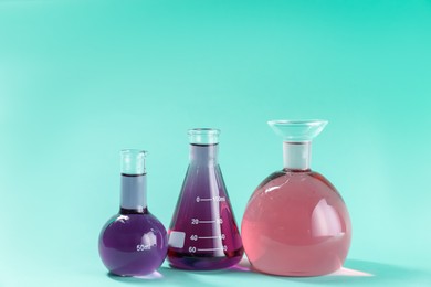 Photo of Laboratory glassware with colorful liquids on turquoise background. Space for text
