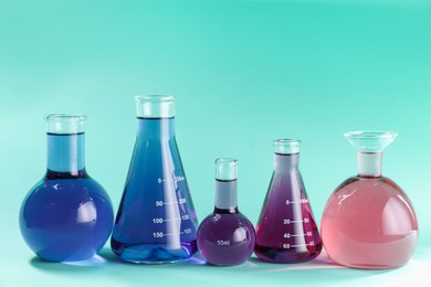 Photo of Laboratory glassware with colorful liquids on turquoise background