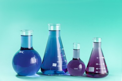 Photo of Laboratory glassware with colorful liquids on turquoise background