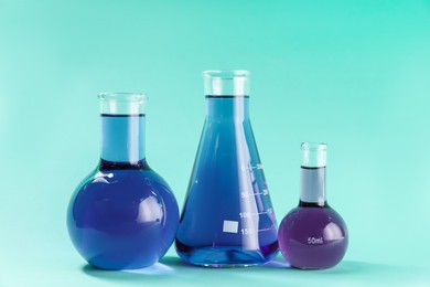 Photo of Laboratory glassware with colorful liquids on turquoise background