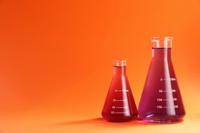 Photo of Laboratory glassware with red liquid on orange background. Space for text