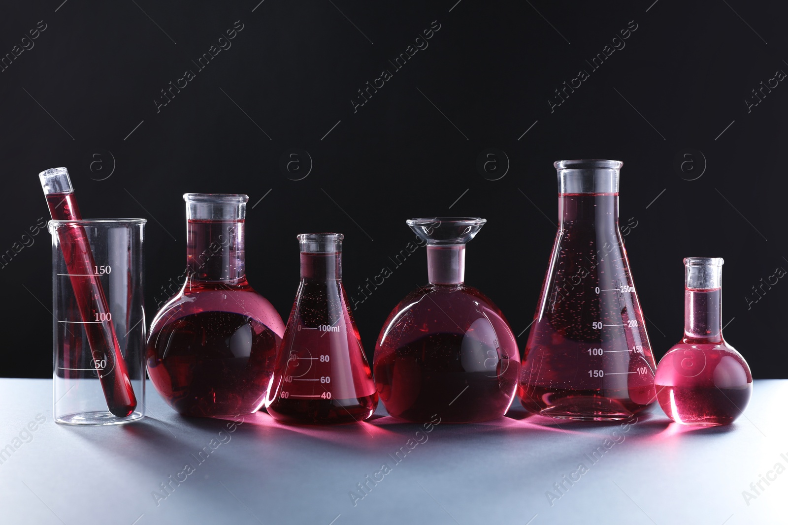 Photo of Laboratory glassware with red liquid on table against black background