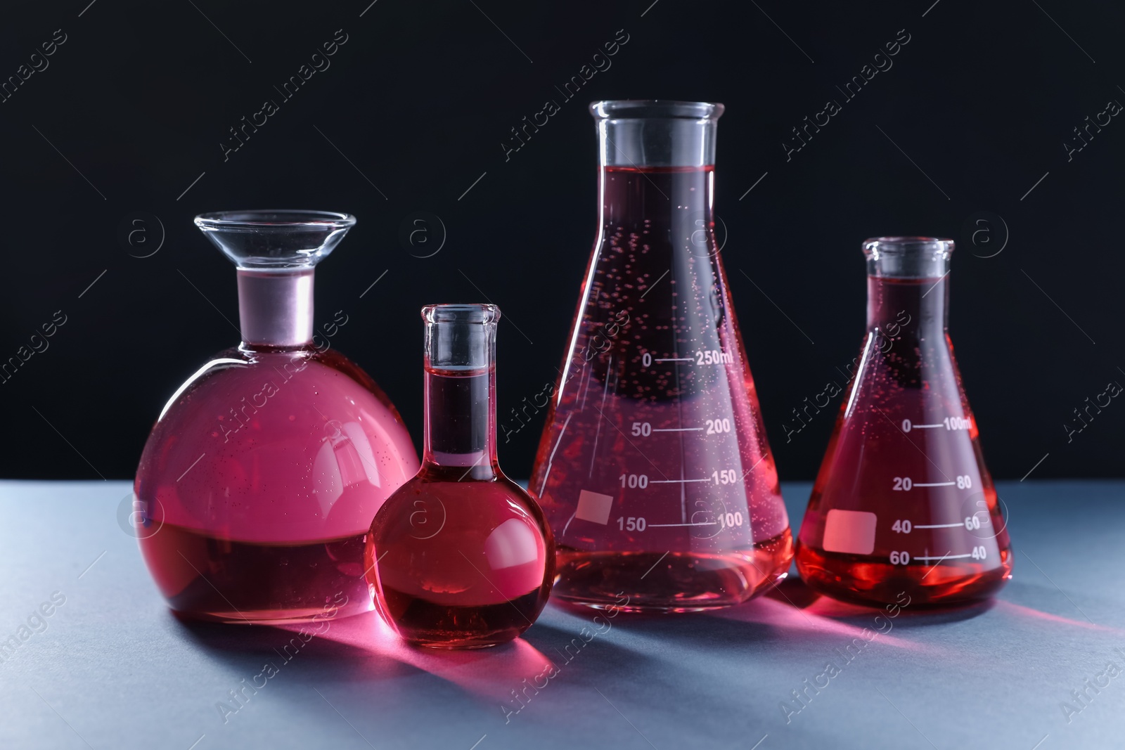 Laboratory glassware with red liquid on table against black background Photo of Laboratory glassware with red liquid on table against black background