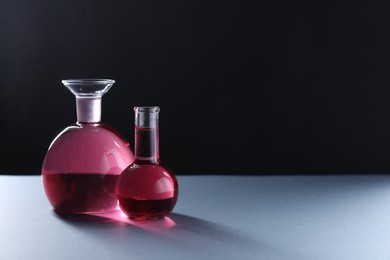 Photo of Laboratory glassware with red liquid on table against black background. Space for text