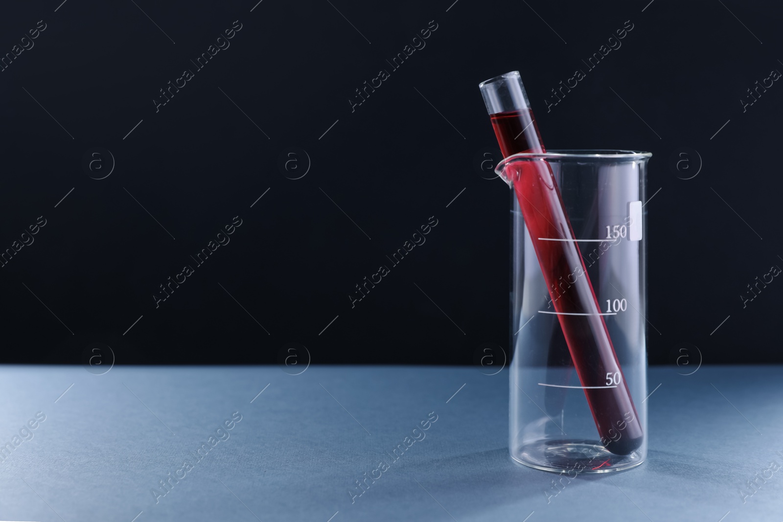 Laboratory glassware with red liquid on table against black background. Space for text Photo of Laboratory glassware with red liquid on table against black background. Space for text