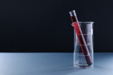 Photo of Laboratory glassware with red liquid on table against black background. Space for text