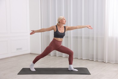 Photo of Mature woman in sportswear stretching on mat near window at home