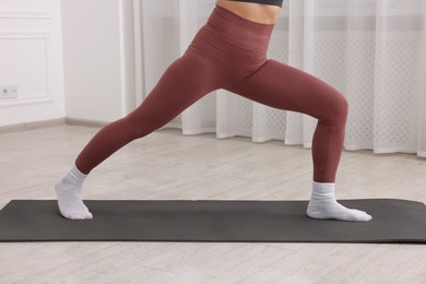 Photo of Mature woman in sportswear stretching on mat at home, closeup