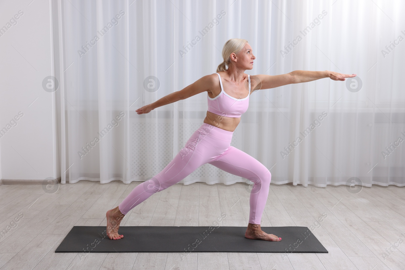 Photo of Mature woman in sportswear stretching on mat near window at home