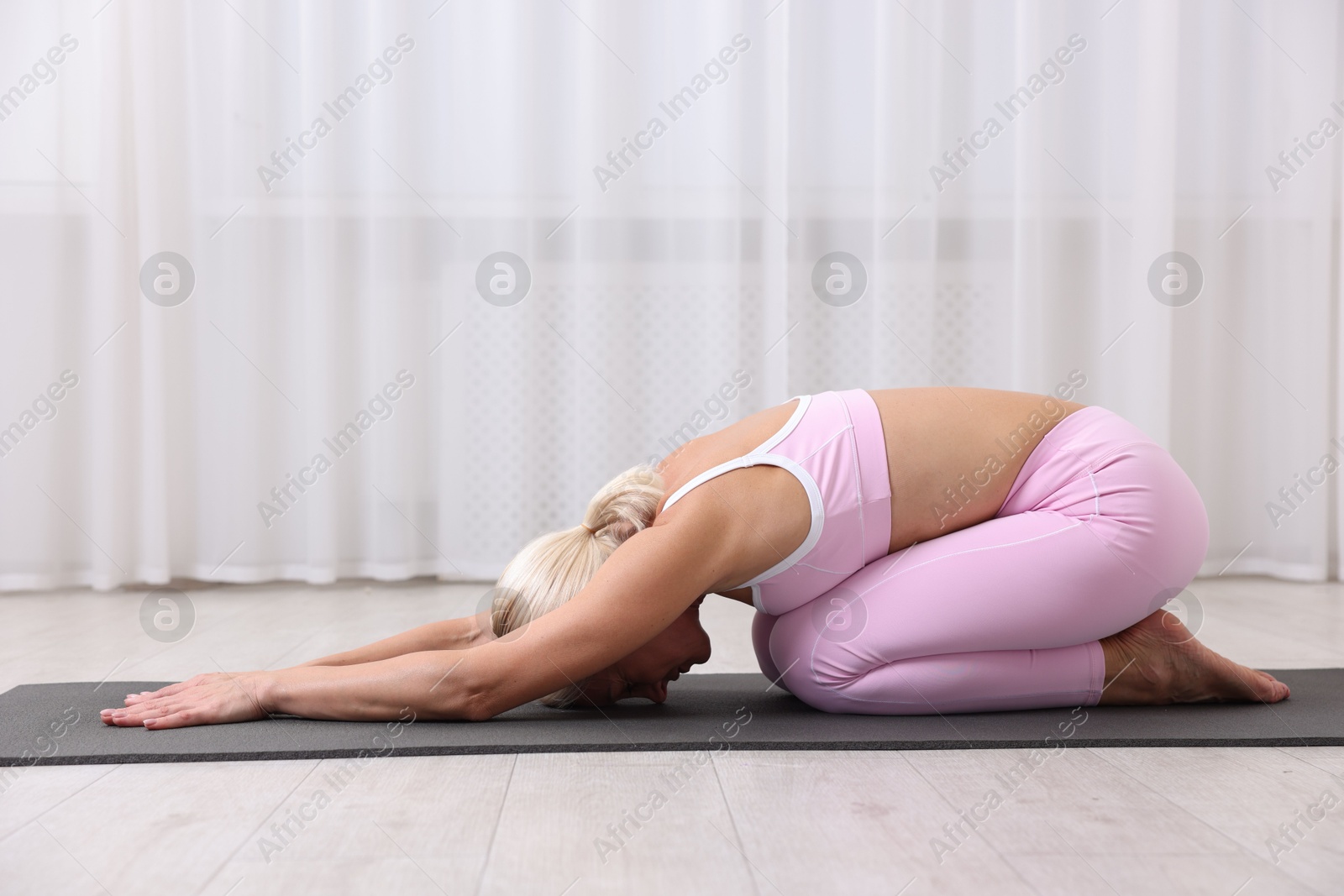 Photo of Mature woman in sportswear stretching on mat at home
