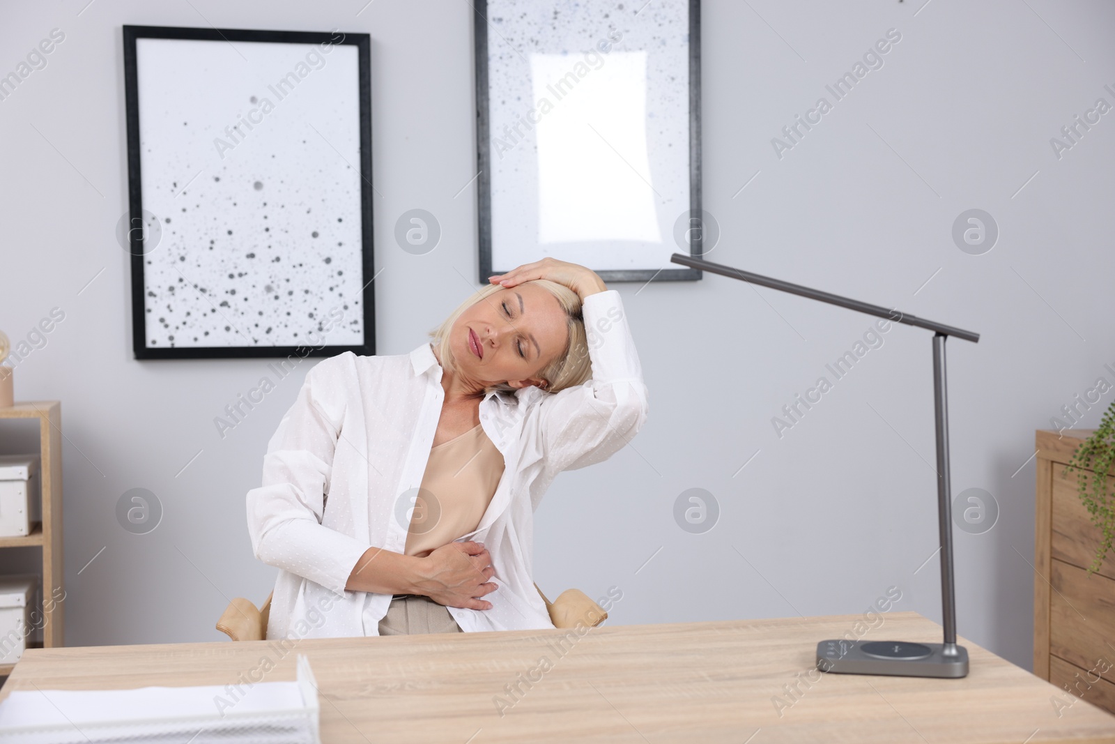 Photo of Mature woman stretching at table near grey wall