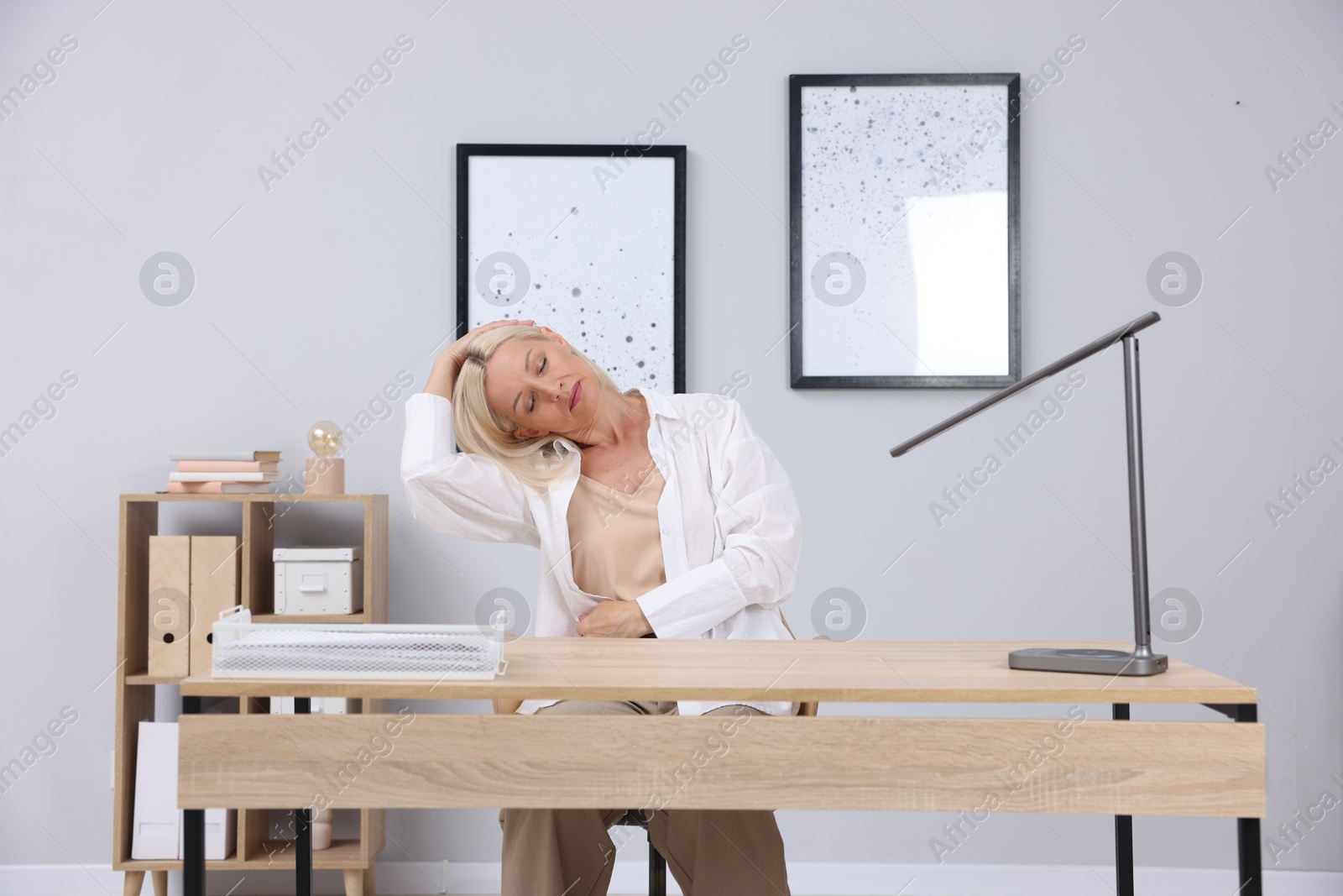 Photo of Mature woman stretching at table near grey wall