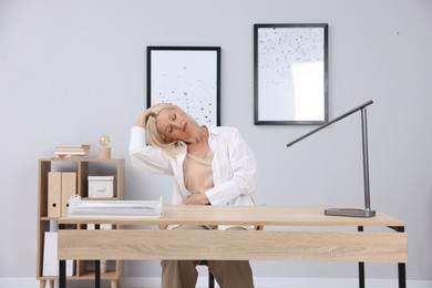 Photo of Mature woman stretching at table near grey wall