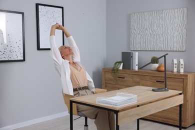 Photo of Mature woman stretching at table near grey wall