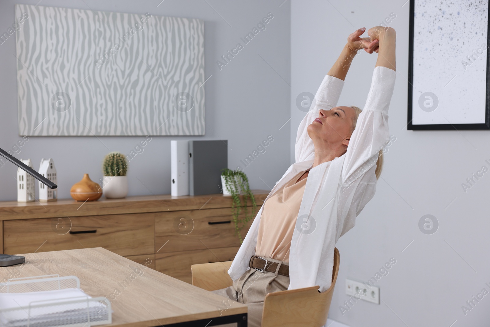 Photo of Mature woman stretching at table near grey wall