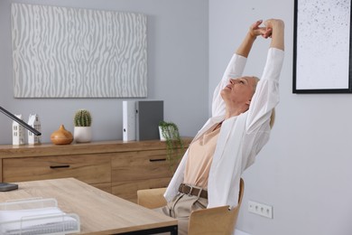 Photo of Mature woman stretching at table near grey wall