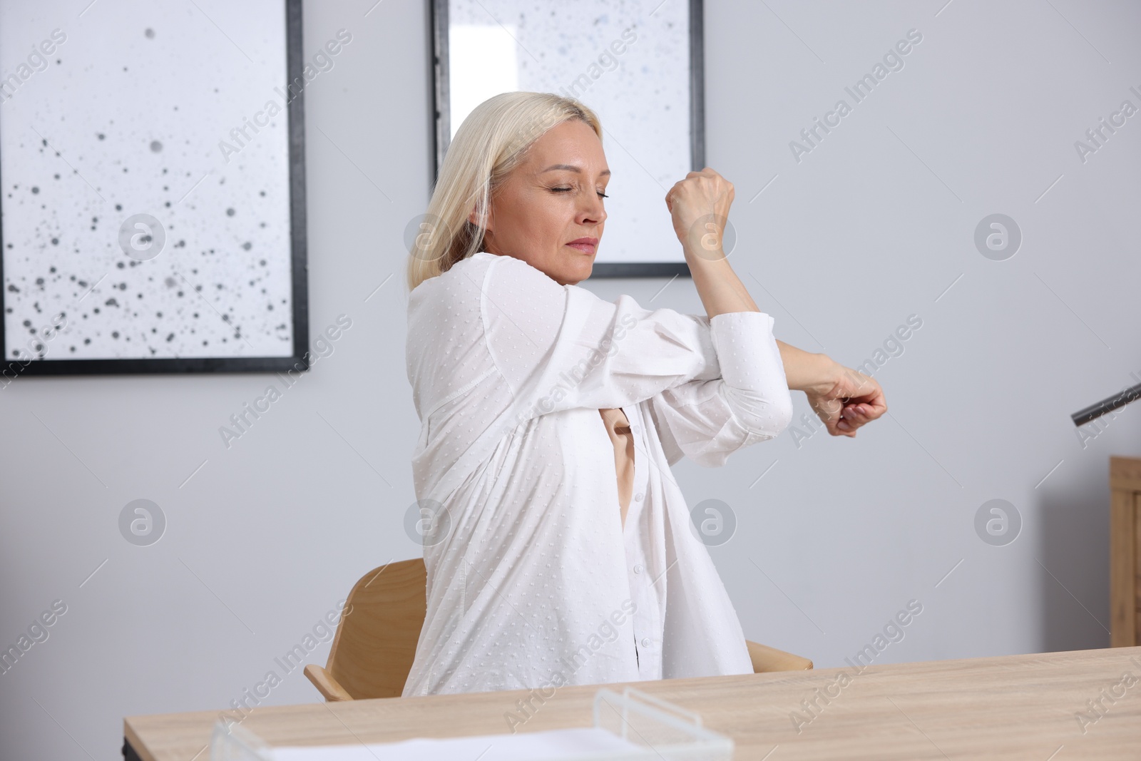 Photo of Mature woman stretching at table near grey wall