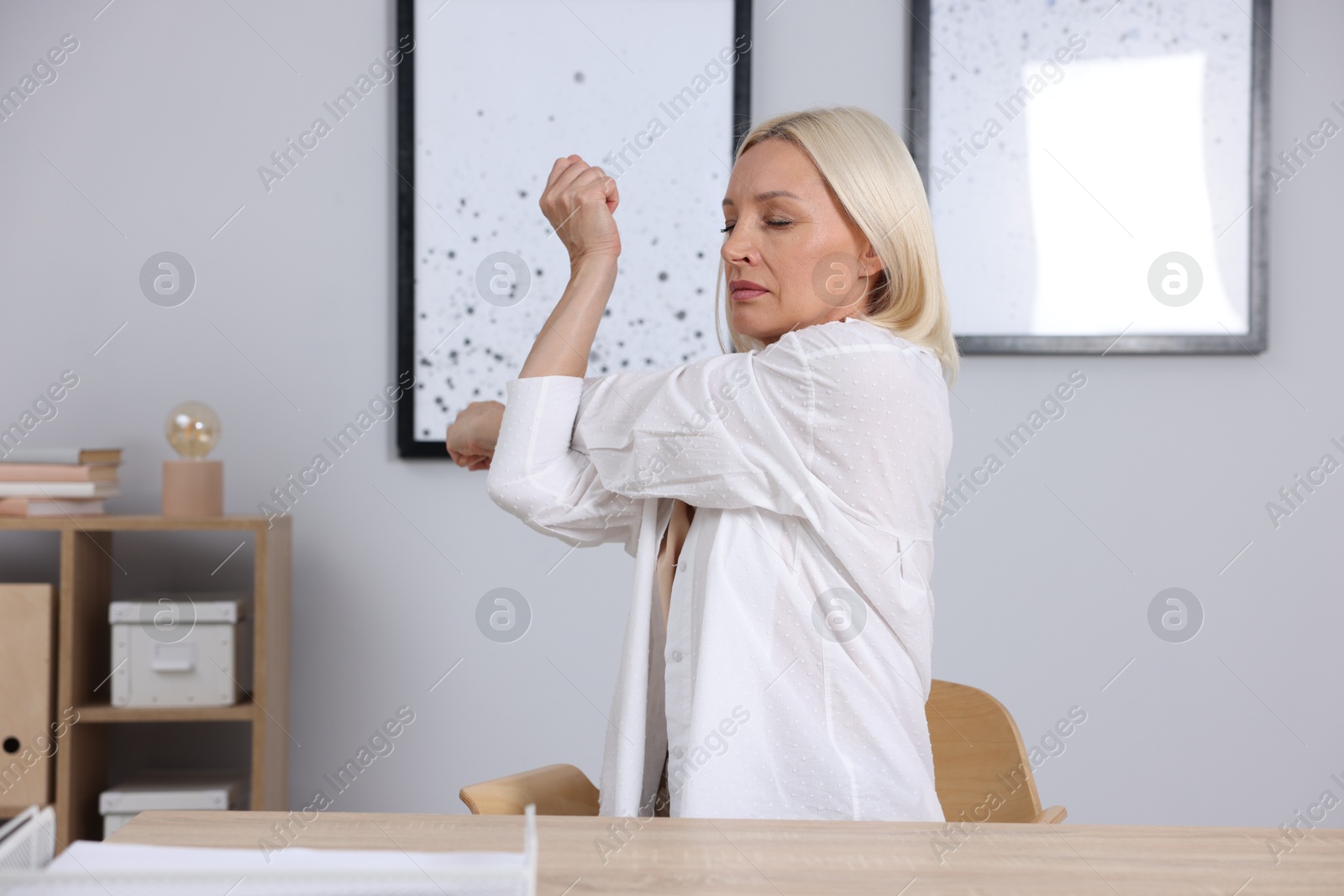 Photo of Mature woman stretching at table near grey wall