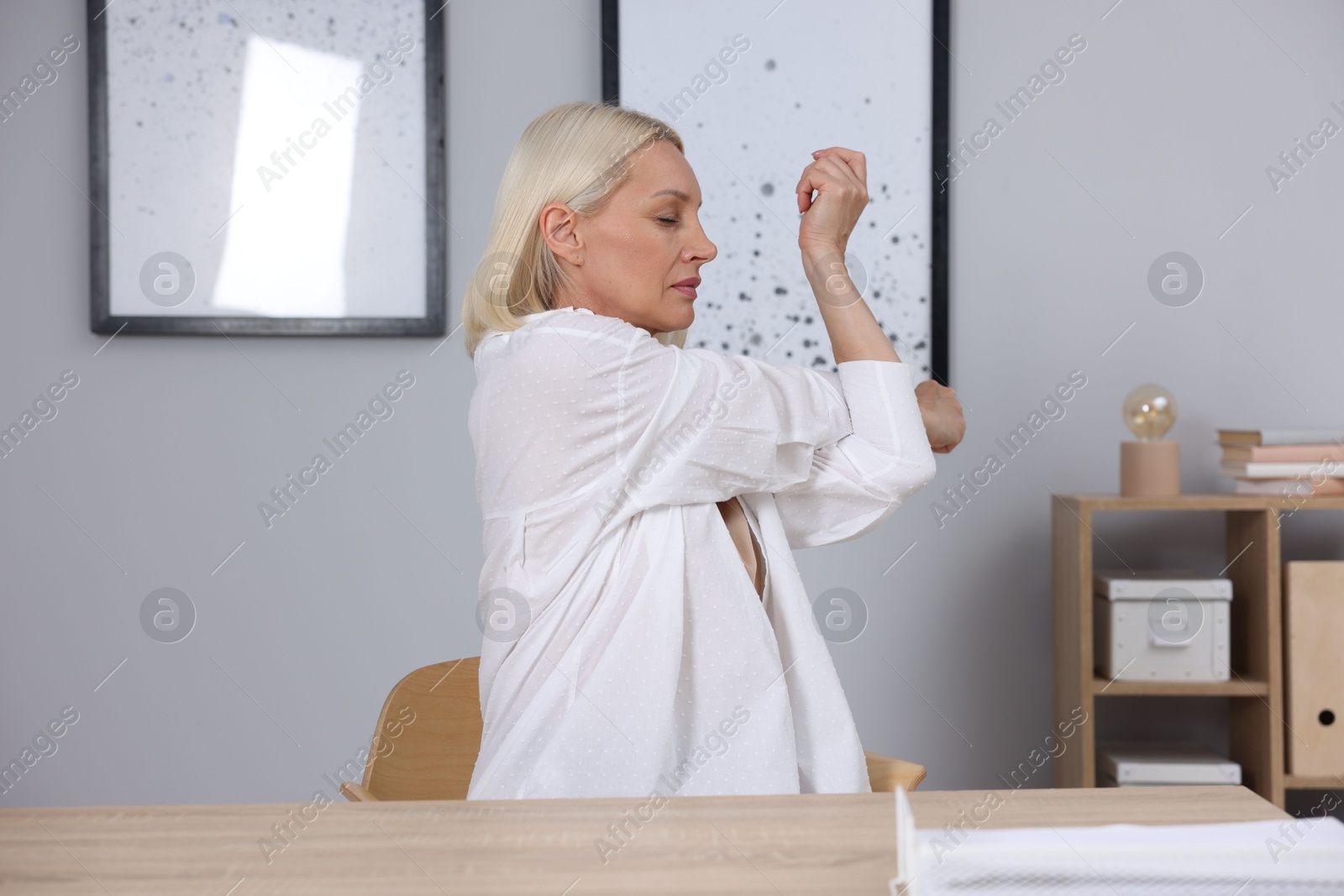 Photo of Mature woman stretching at table near grey wall