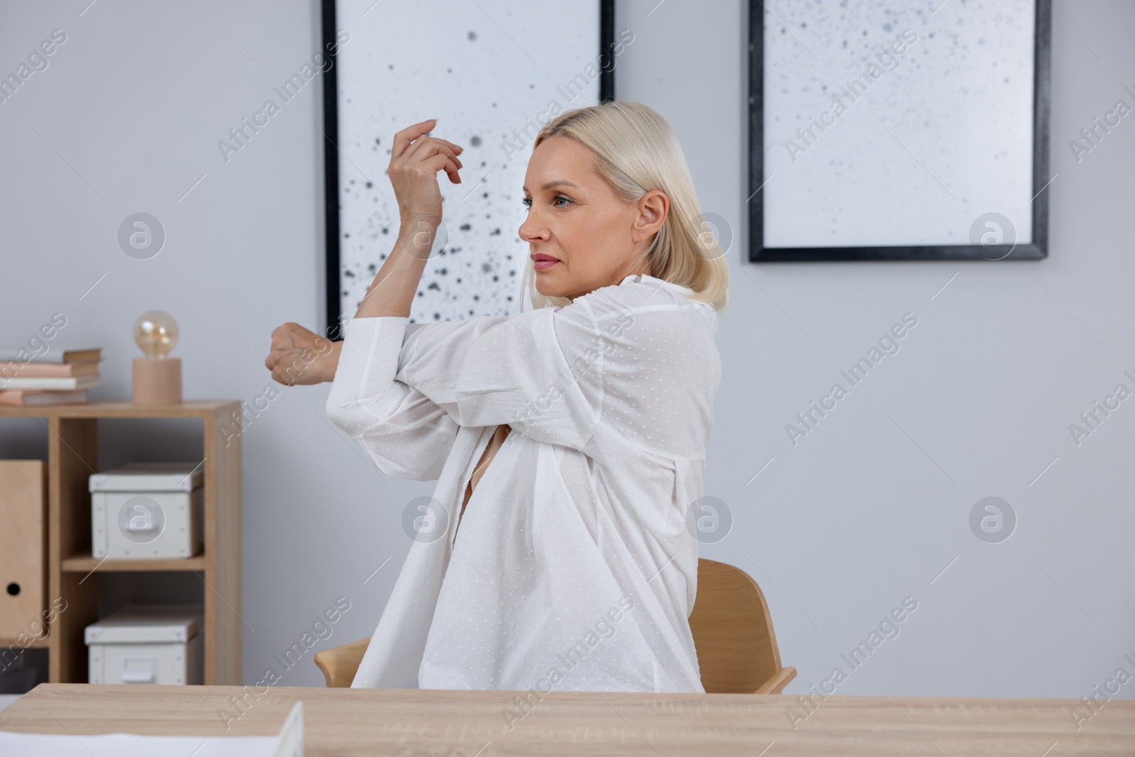 Photo of Mature woman stretching at table near grey wall