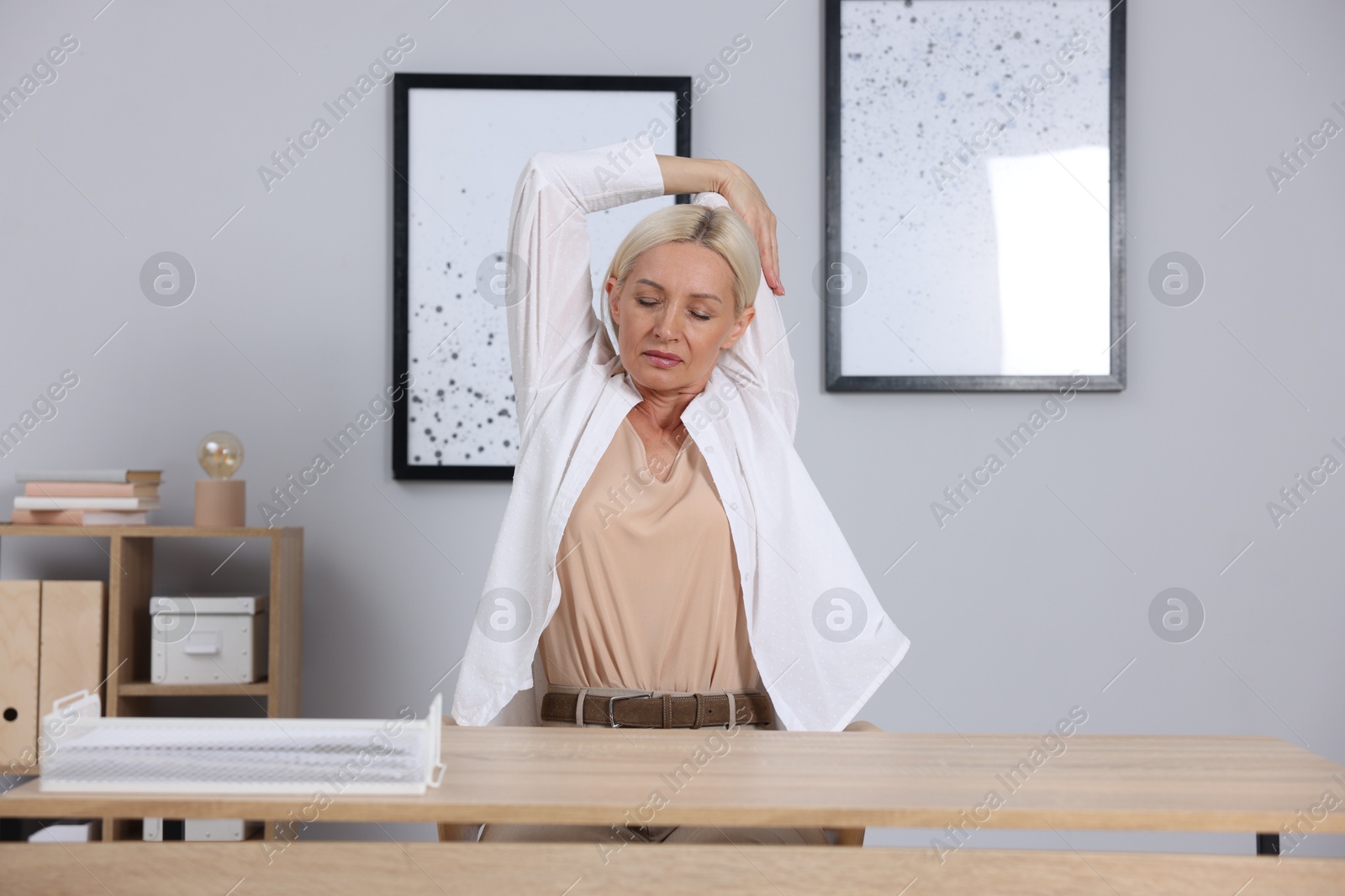 Photo of Mature woman stretching at table near grey wall