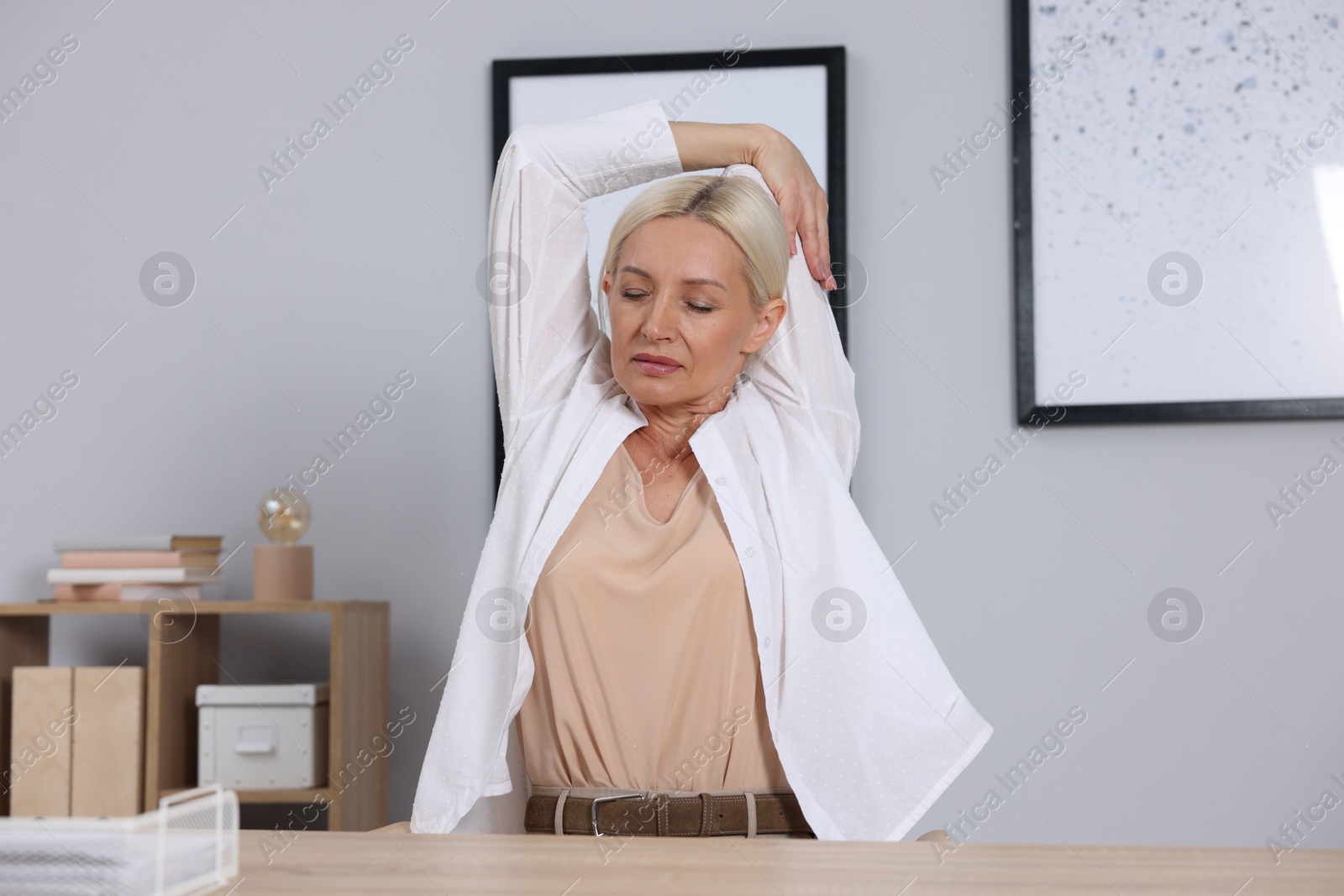 Photo of Mature woman stretching at table near grey wall
