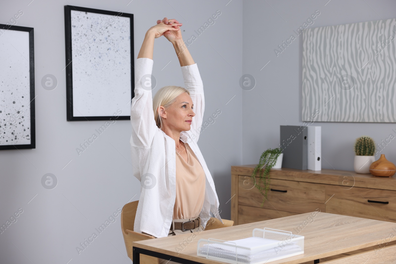 Photo of Mature woman stretching at table near grey wall