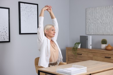 Photo of Mature woman stretching at table near grey wall