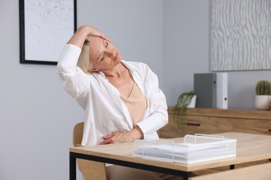 Photo of Mature woman stretching at table near grey wall