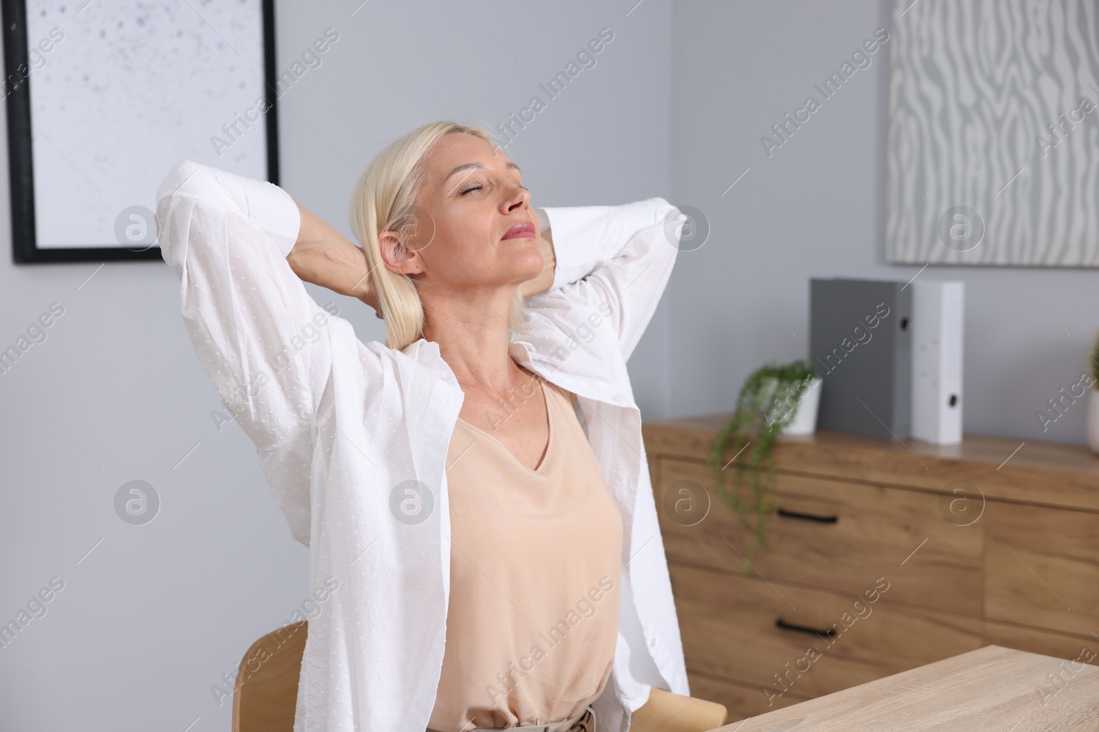 Photo of Mature woman stretching at workplace near grey wall