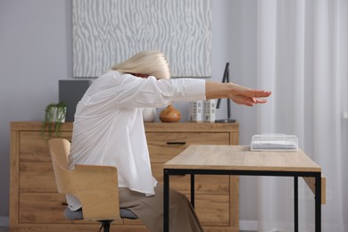 Photo of Mature woman stretching at table in office