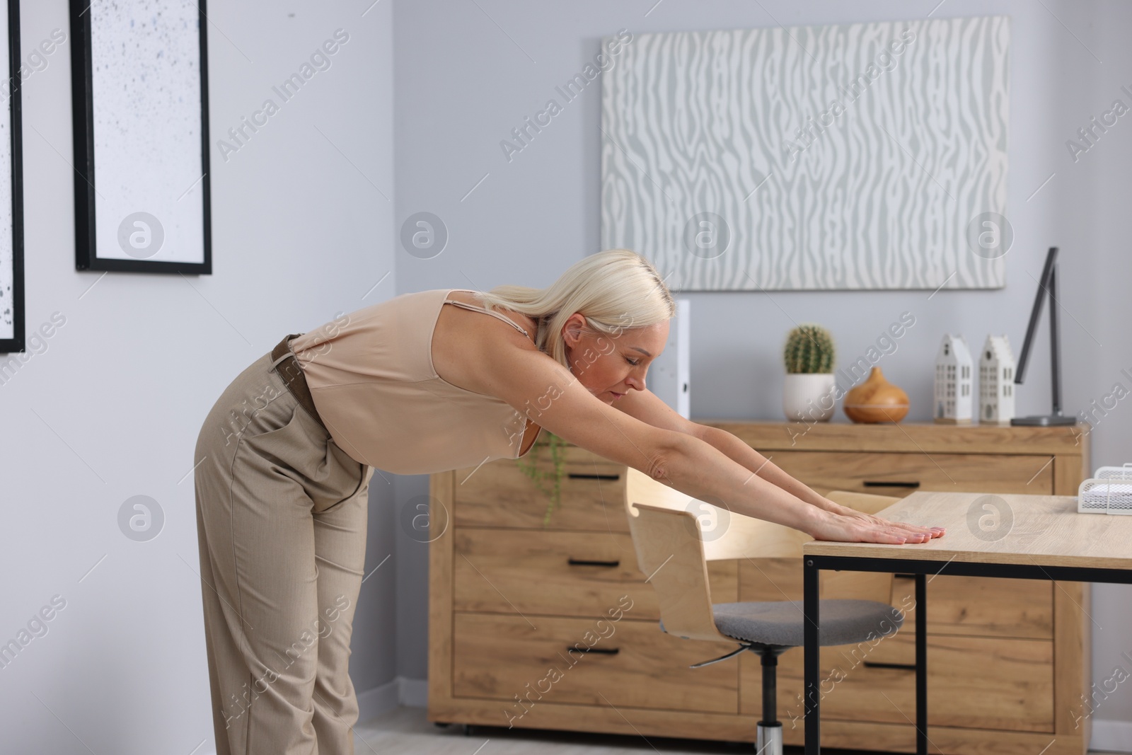 Photo of Mature woman stretching leaning on table in office