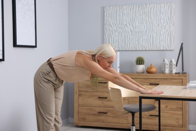 Photo of Mature woman stretching leaning on table in office
