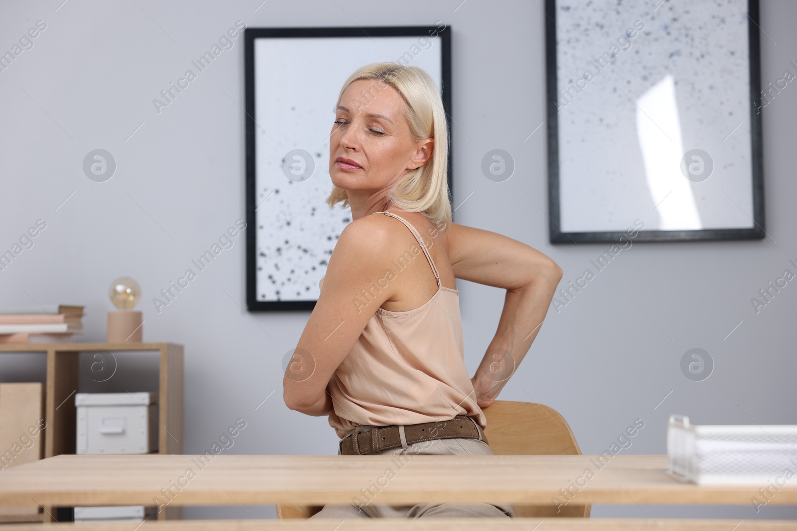 Photo of Mature woman stretching at table near grey wall