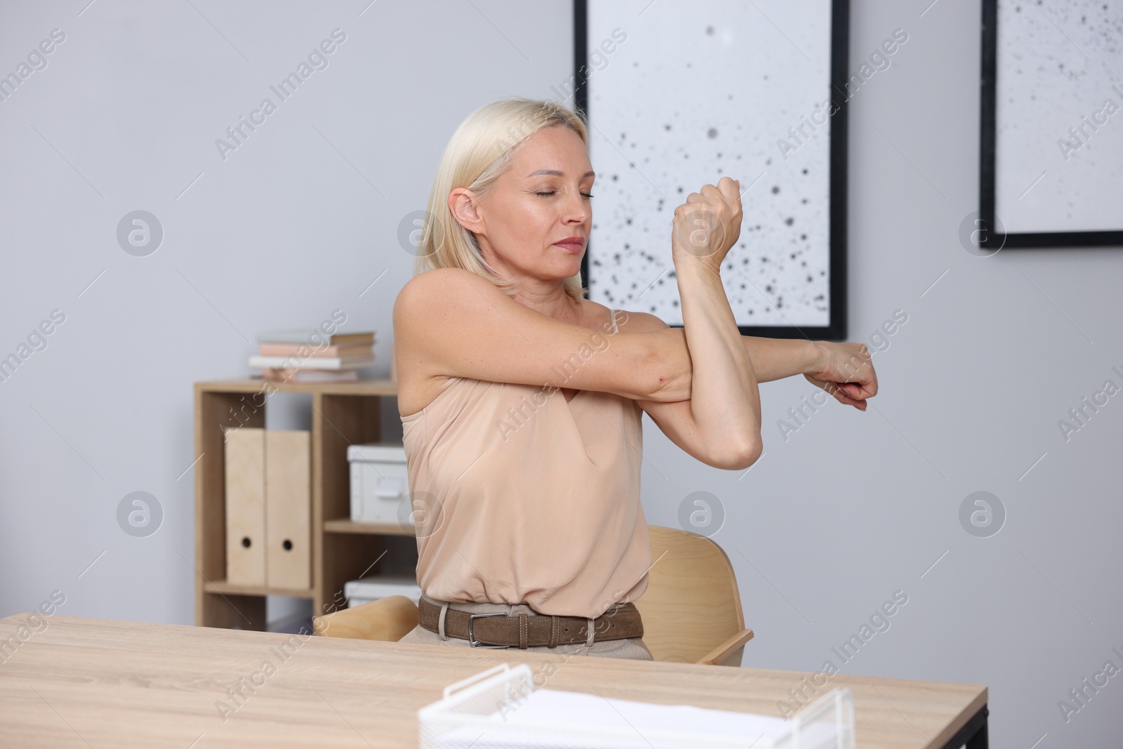 Photo of Mature woman stretching at table near grey wall