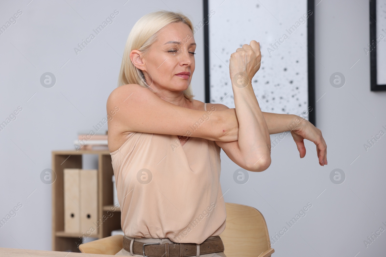 Photo of Mature woman stretching at workplace near grey wall