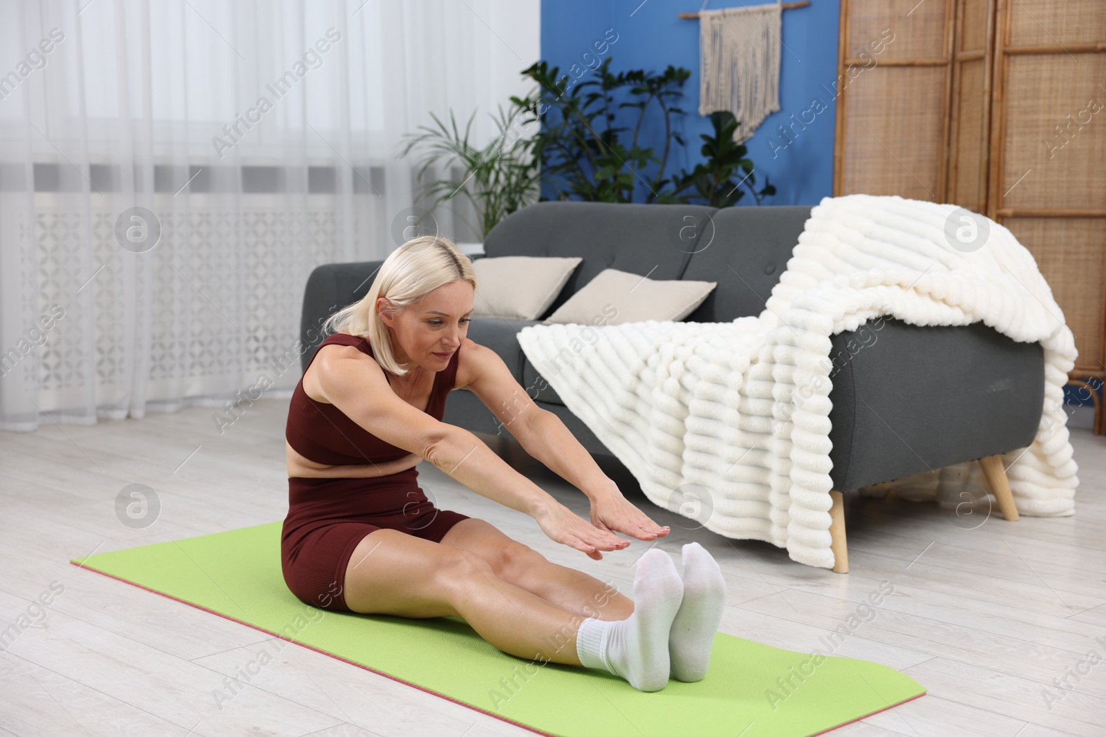 Photo of Mature woman in sportswear stretching on mat at home