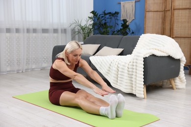 Photo of Mature woman in sportswear stretching on mat at home