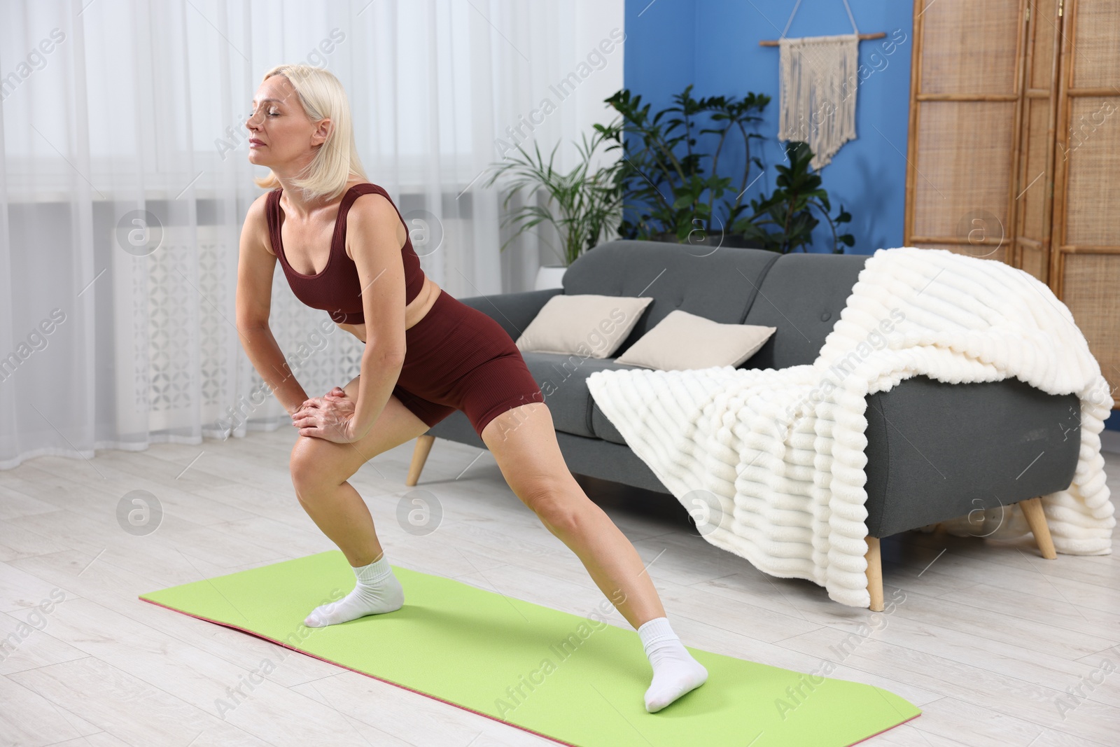 Photo of Mature woman in sportswear stretching on mat at home