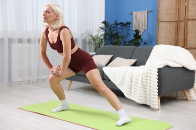 Photo of Mature woman in sportswear stretching on mat at home