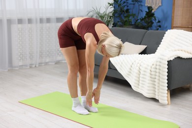 Photo of Mature woman in sportswear stretching on mat at home