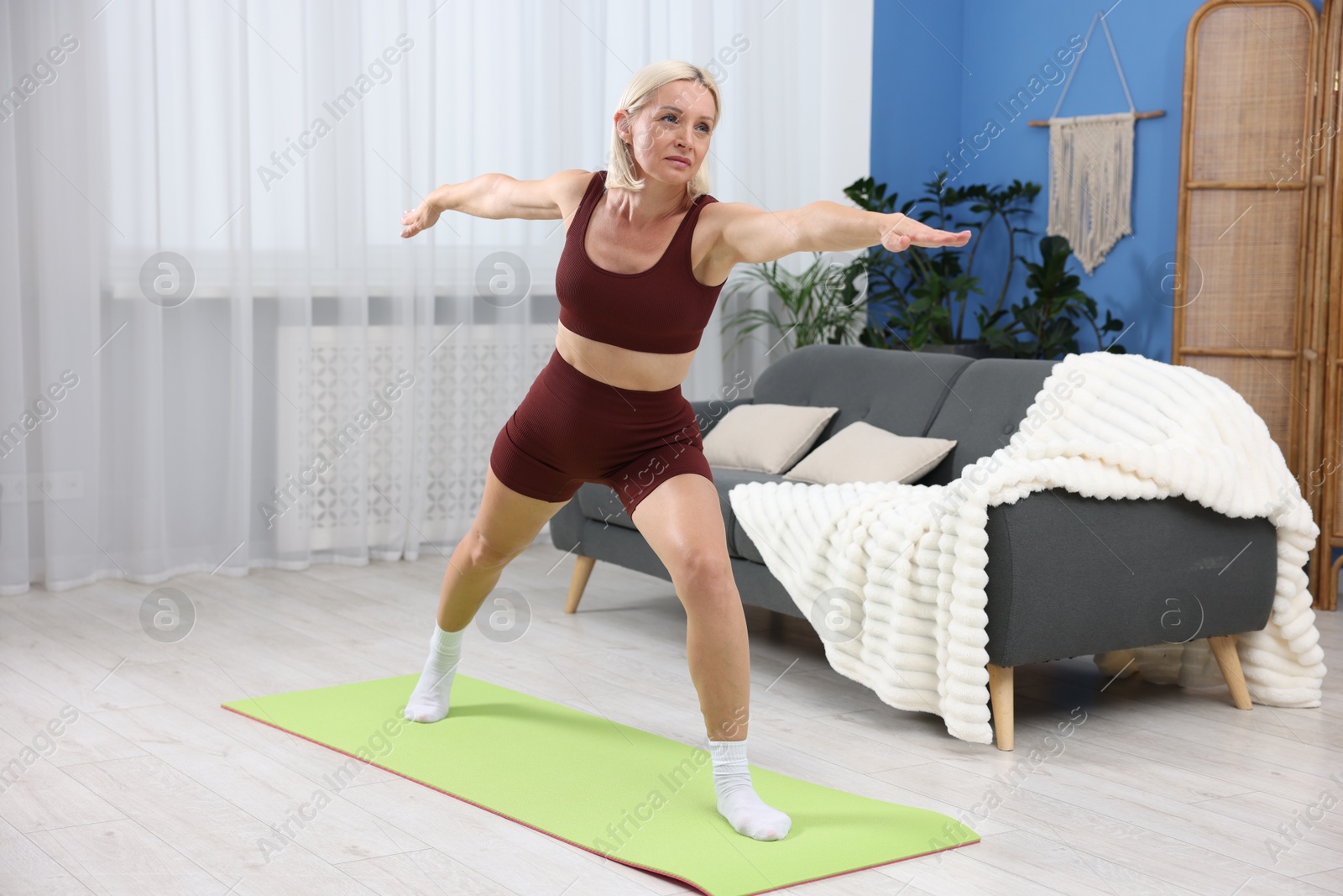 Photo of Mature woman in sportswear stretching on mat at home